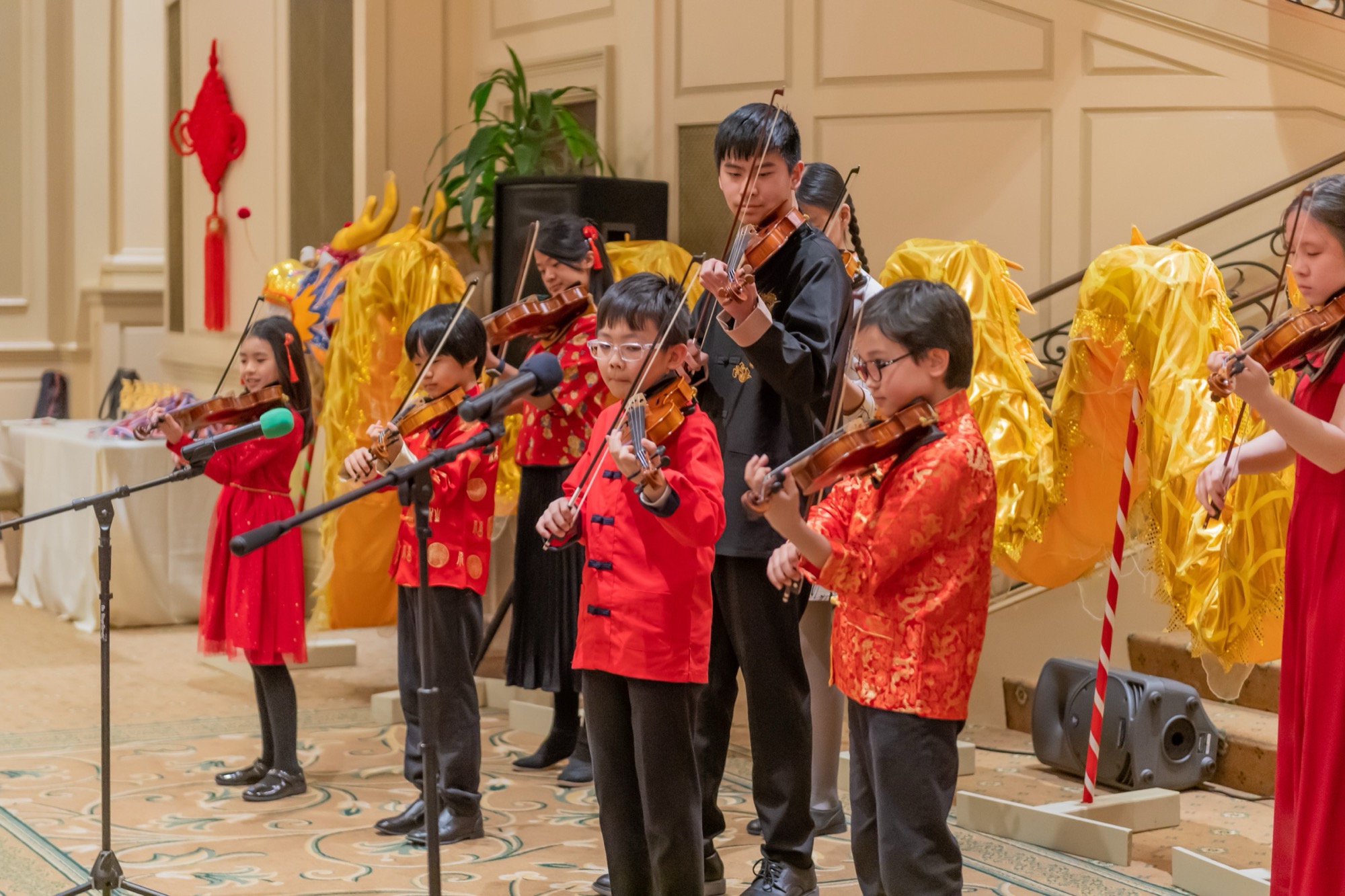 Young violinists in red performing in front of a gold dragon